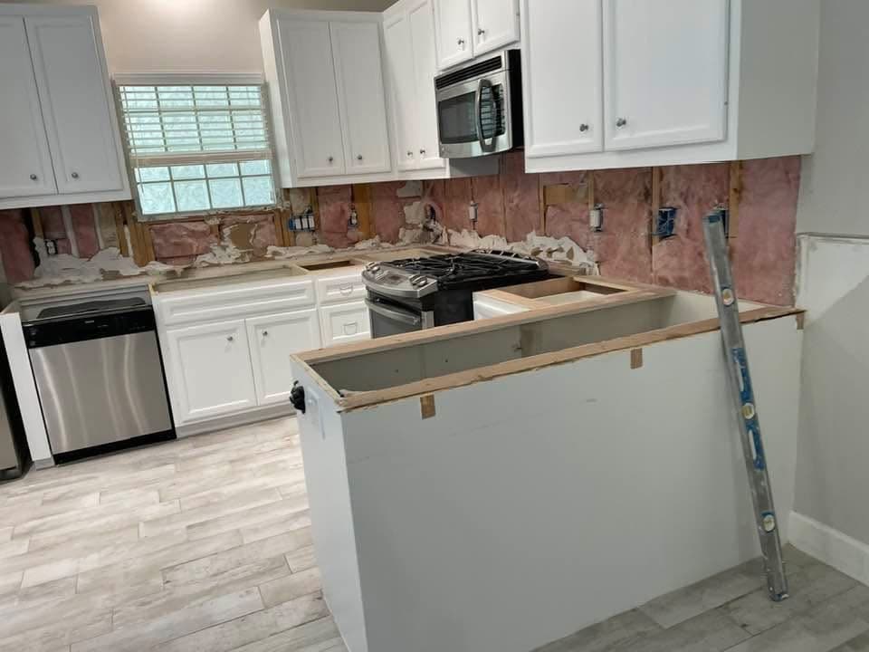 Cocina con el respaldo de pared retirado hasta el aislante y la isla en obra gris, sin encimera